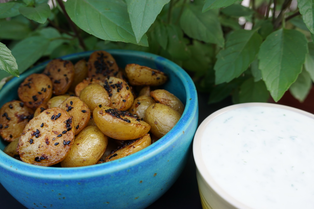 Kartoffeln mit schwarzen Sesam in einer blauen Schüssel, daneben eine weiße Schüssel mit Joghurt